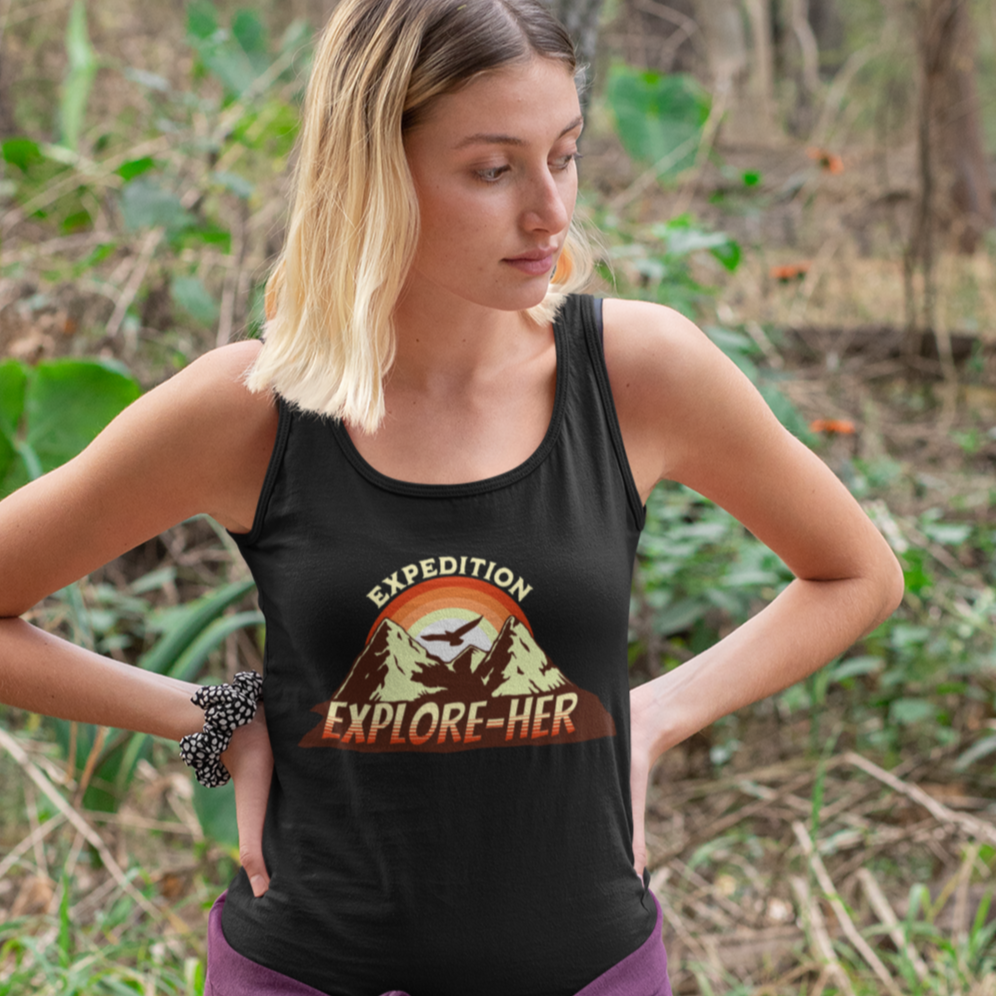 Funny lesbian tank top featuring "Expedition Explore-HER" in bold, playful text – Designed by Queer Energy- mockup of blonde lesbian wearing a black tank top in a forest setting