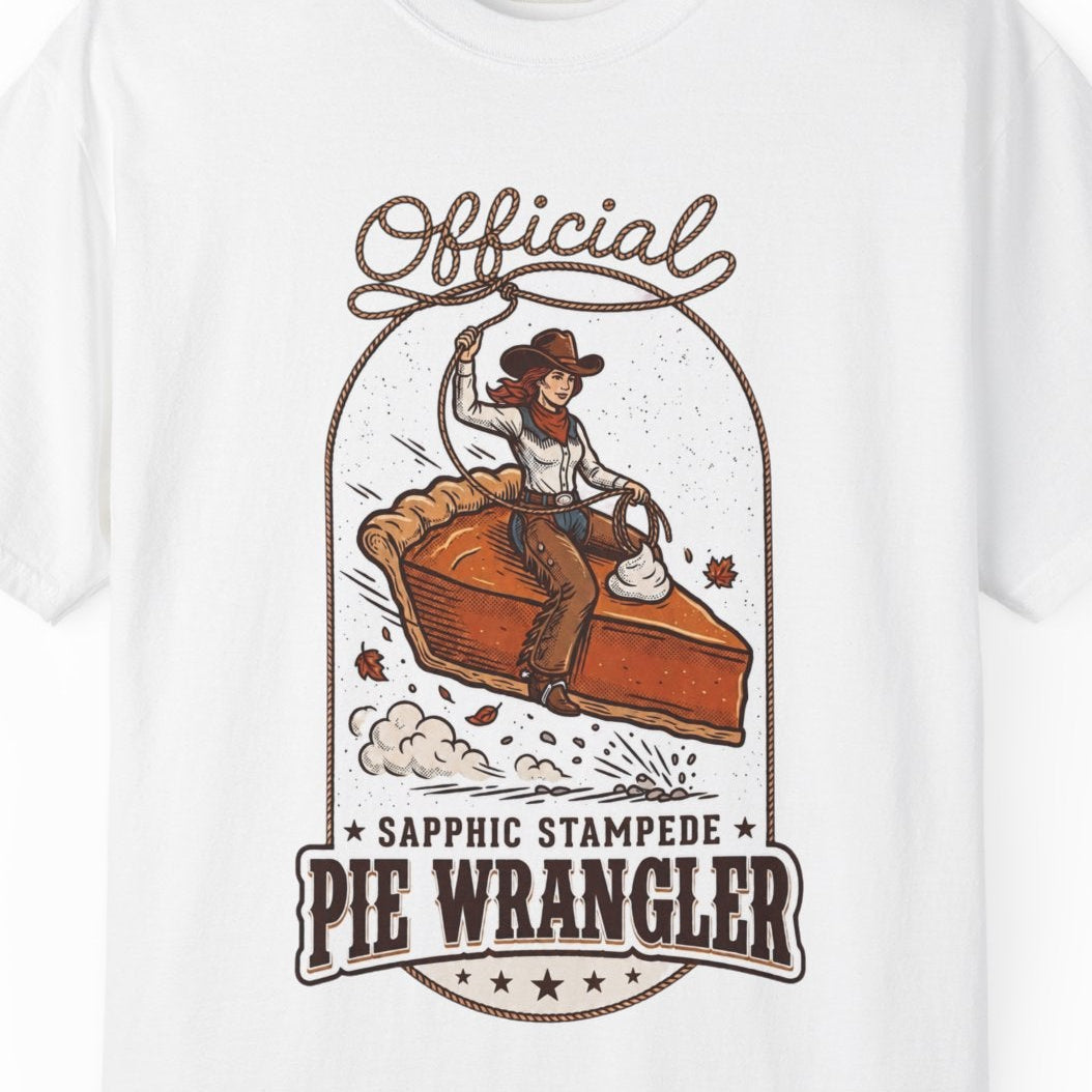 A white short-sleeve crewneck t-shirt featuring a vintage-style graphic of a cowgirl riding a pie, with the text 'Official Sapphic Stampede Pie Wrangler' printed in brown and orange.