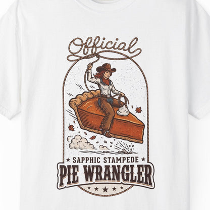 A white short-sleeve crewneck t-shirt featuring a vintage-style graphic of a cowgirl riding a pie, with the text 'Official Sapphic Stampede Pie Wrangler' printed in brown and orange.