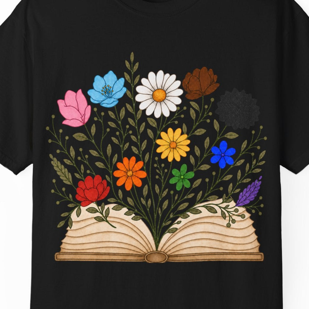 A black short-sleeve crewneck t-shirt featuring a graphic print of an open book with colorful LGBTQ colored flowers blooming from it, displayed on a clean white background.