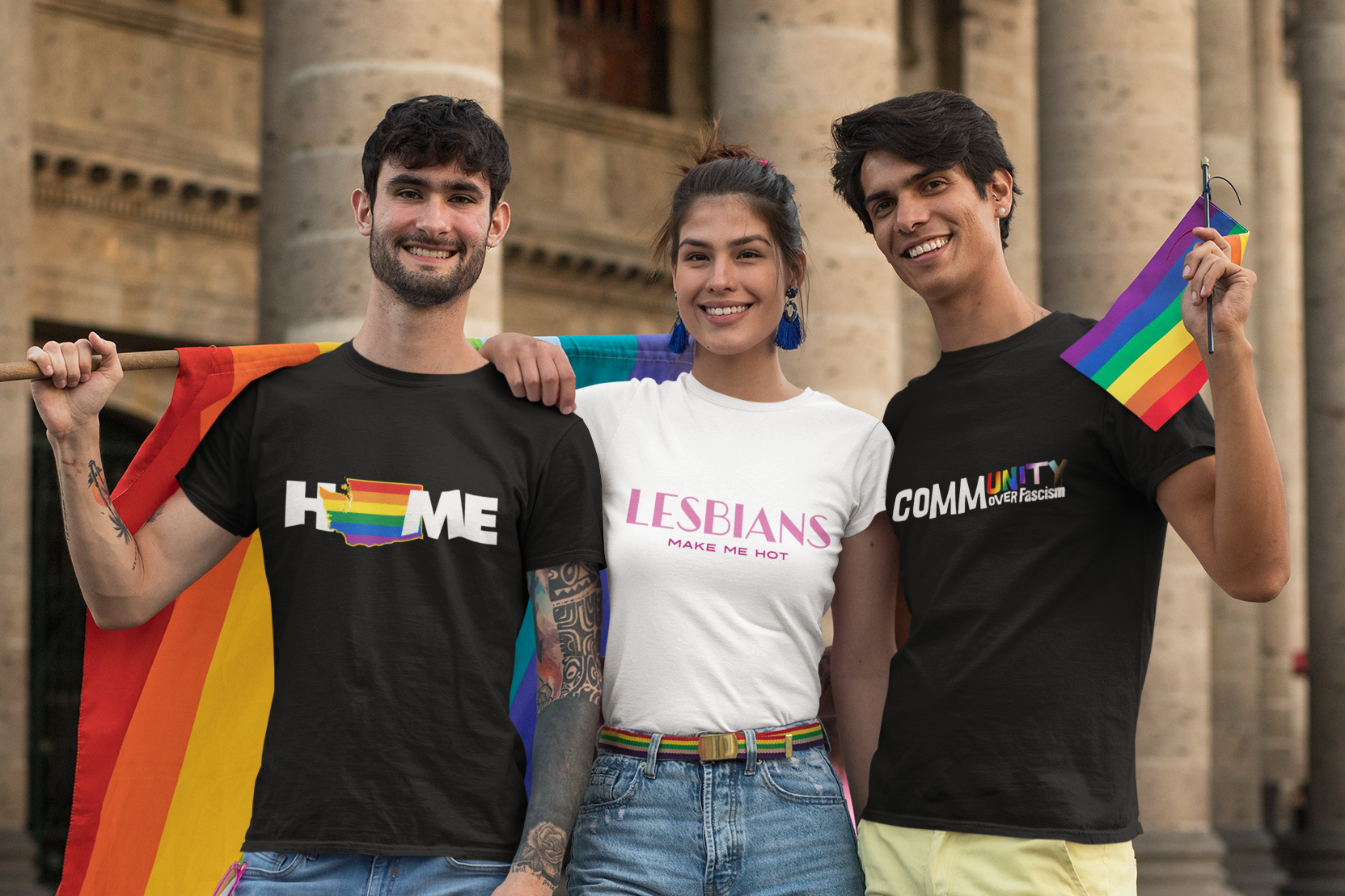 3 LGBTQ Friends holding rainbow flags and pride-themed shirts, by Queer Energy in front of a building with columns.