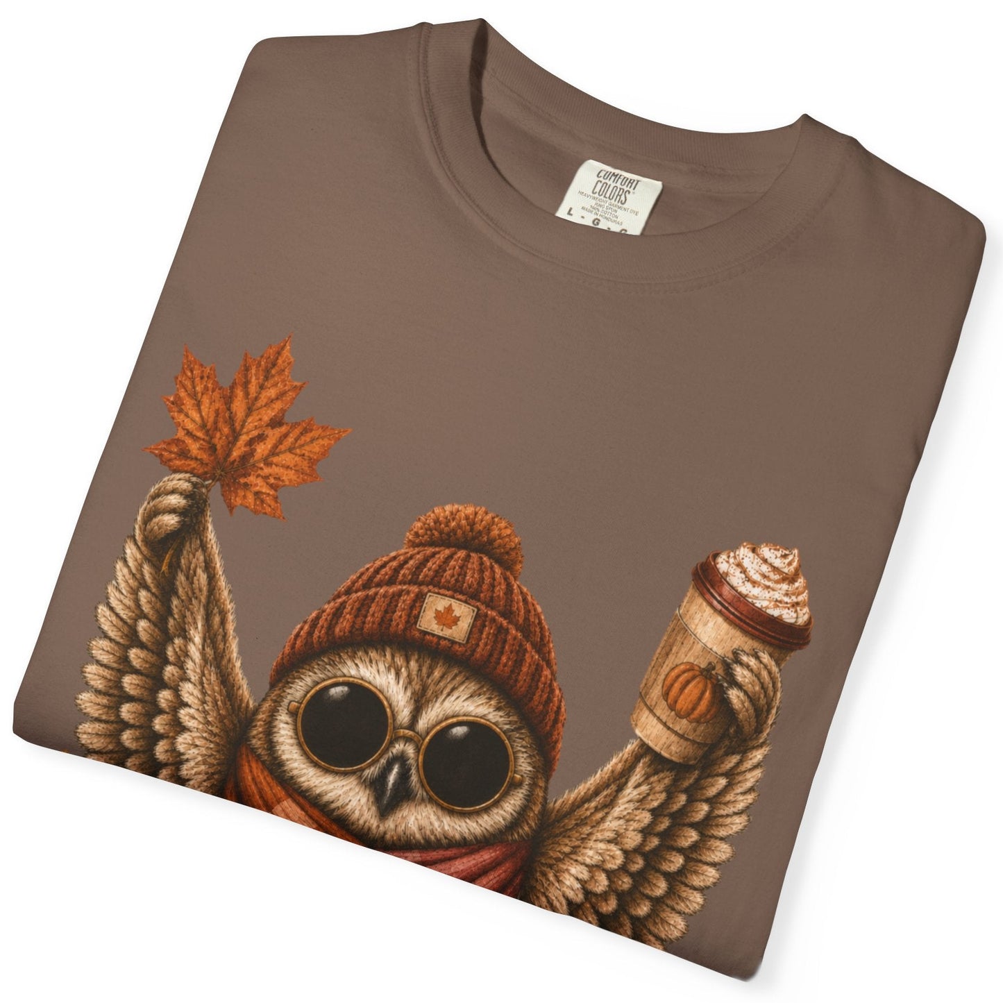 A folded espresso colored short-sleeve crewneck t-shirt featuring a detailed graphic of a cute owl wearing a knit beanie and a lesbian flag-colored plaid scarf, holding a hot drink. The graphic is decorated with autumn leaves, pumpkins, and the text 'Sapphic Season' at the bottom.