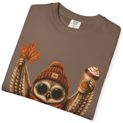 A folded espresso colored short-sleeve crewneck t-shirt featuring a detailed graphic of a cute owl wearing a knit beanie and a lesbian flag-colored plaid scarf, holding a hot drink. The graphic is decorated with autumn leaves, pumpkins, and the text 'Sapphic Season' at the bottom.