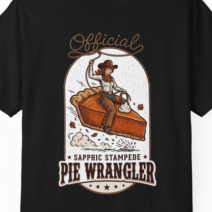 A black short-sleeve crewneck t-shirt featuring a vintage-style graphic of a cowgirl riding a pie, with the text 'Official Sapphic Stampede Pie Wrangler' printed in brown and orange.