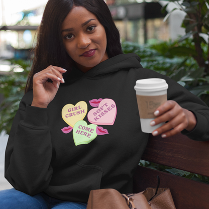 Sapphic sitting on a bench wearing a black valentine's hoodie with colorful text, holding a coffee cup.