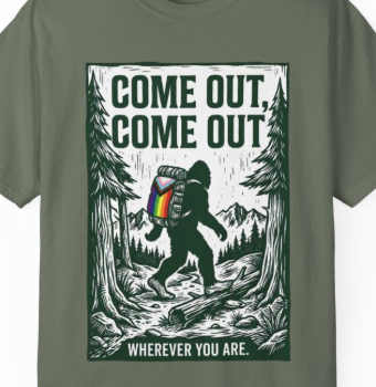 An olive green short-sleeve t-shirt with a large graphic print on the front. The graphic features a black and white illustration of a bigfoot carrying a colorful rainbow backpack in a forest, with the text 'COME OUT, COME OUT' above and 'WHEREVER YOU ARE.