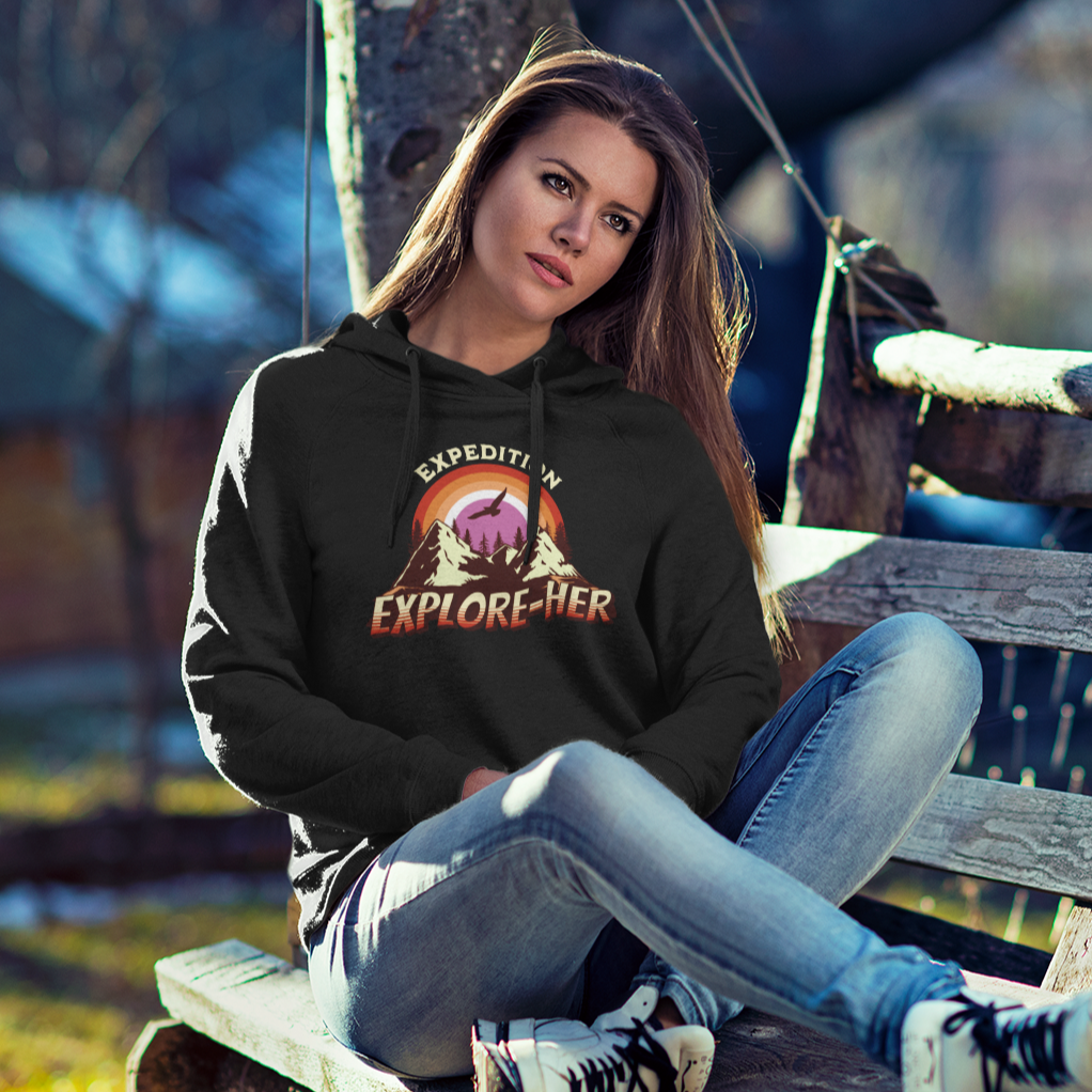 Gay pride hoodie featuring Expedition Explore-HER funny lesbian LGBTQ+ pun design – Designed by Queer Energy mockup of lesbian wearing black hoodie sitting on a bench outside