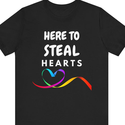 Black Tee that says “Here to Steal Hearts” in white text with a rainbow ribbon forming a heart beneath – Designed by Queer Energy