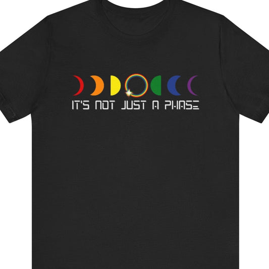LGBTQ Pride black tee that says “IT’S NOT JUST A PHASE” in bold rainbow lettering – Designed by Queer Energy 