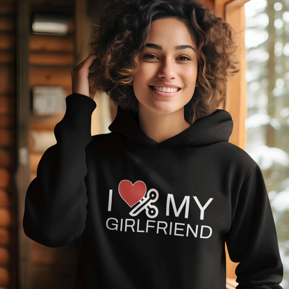 Lesbian wearing a black hoodie with 'I ❤️ MY GIRLFRIEND' text, standing indoors with a snowy outdoor view.