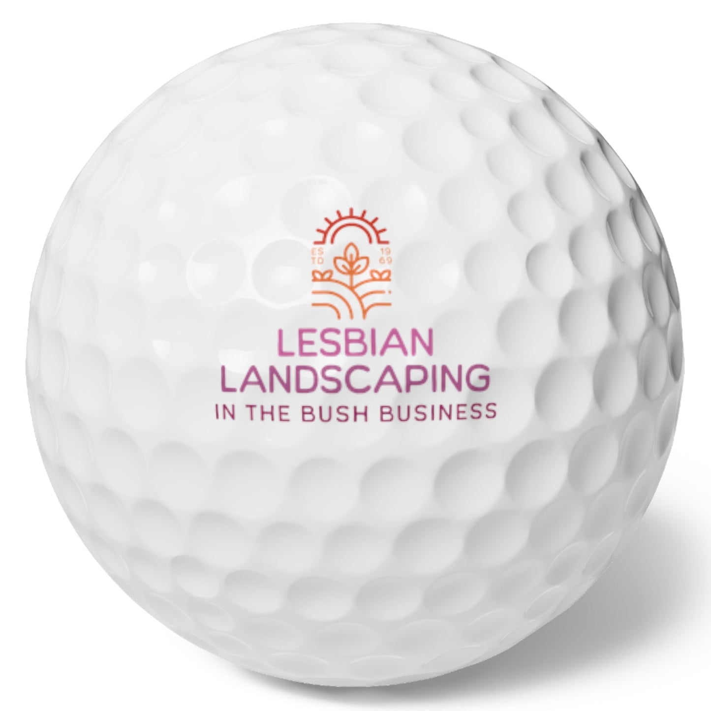 White golf ball that says: Lesbian Landscaping - In the bush business in Lesbian flag colors