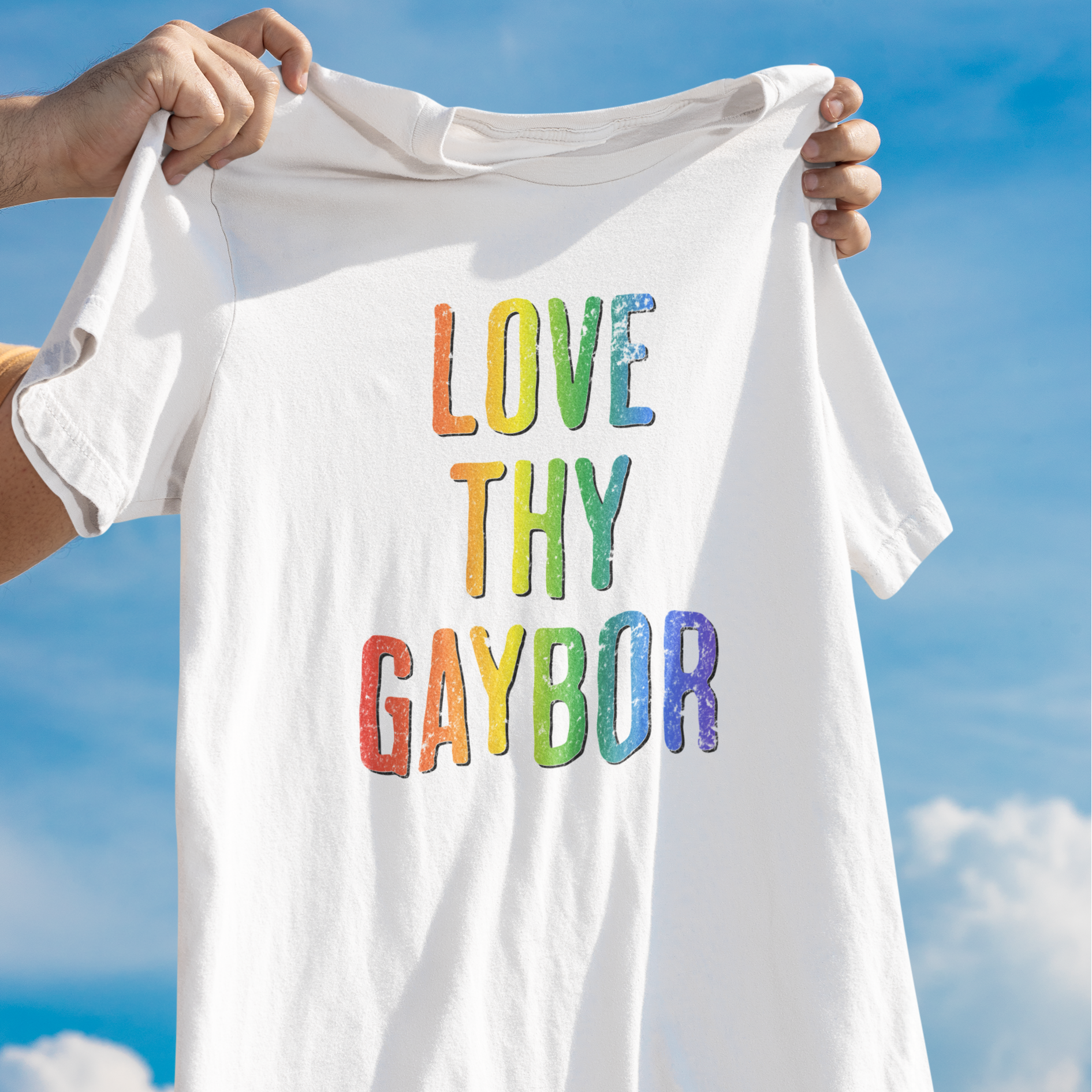 White t-shirt with 'LOVE THY GAYBOR' in rainbow letters held against a blue sky.