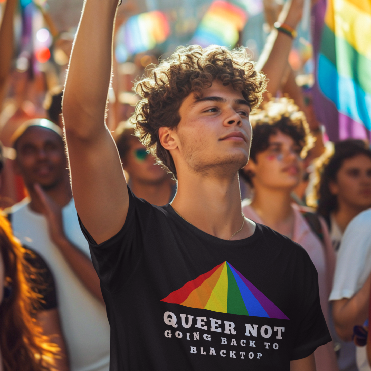 Gay man wearing a black t-shirt with a rainbow design and white text, surrounded by people holding pride flags in an outdoor setting.