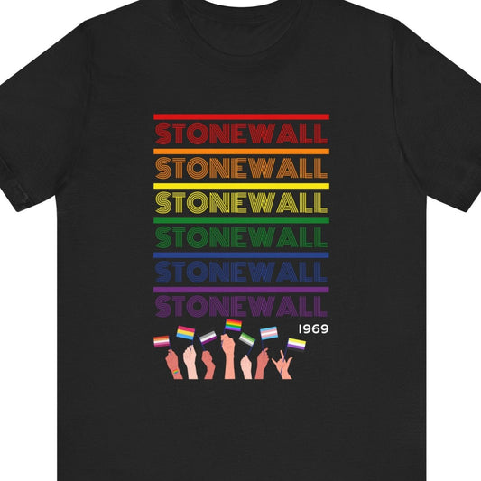 Black Tee that says “Stonewall 1969” in LGBTQ rainbow colors with a hand holding diverse Pride flags – Designed by Queer Energy