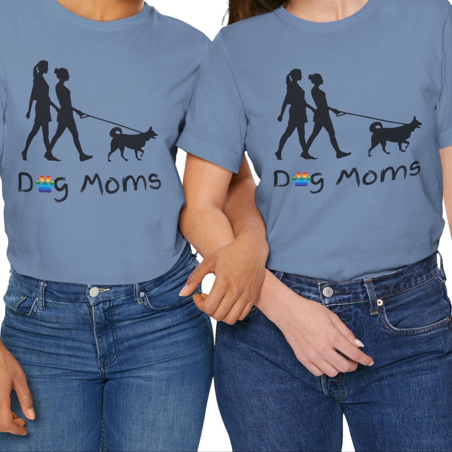 mockup of two lesbians wearing steam blue LGBTQ Pride tee that says “Dog Moms” with a rainbow paw print and a silhouette of two lesbians walking a dog – Designed by Queer Energy