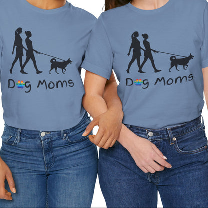 mockup of two lesbians wearing steam blue LGBTQ Pride tee that says “Dog Moms” with a rainbow paw print and a silhouette of two lesbians walking a dog – Designed by Queer Energy